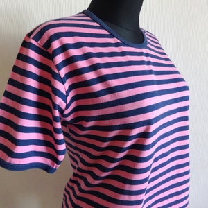 K&ouml;nnte beinhalten: Ein pinkfarbenes und marineblaues gestreiftes T-Shirt mit kurzen &Auml;rmeln.