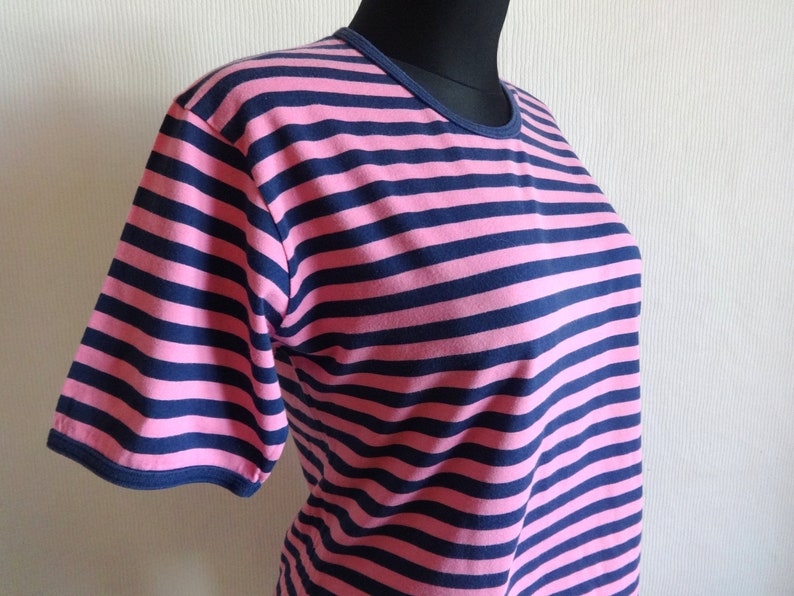 K&ouml;nnte beinhalten: Ein pinkfarbenes und marineblaues gestreiftes T-Shirt mit kurzen &Auml;rmeln.