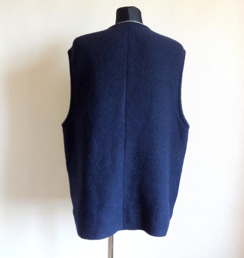 Puede incluir: Un chaleco de punto azul oscuro sin mangas con un ribete blanco alrededor del cuello.