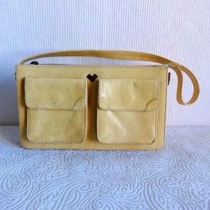May include: A yellow leather handbag with two large front pockets and a heart-shaped detail on the front.
