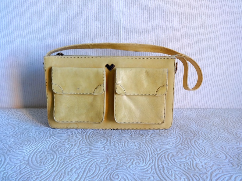May include: A yellow leather handbag with two large front pockets and a heart-shaped detail on the front.