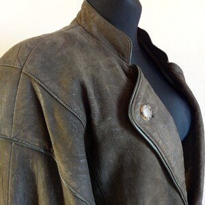 Puede incluir: Una chaqueta de cuero marr&oacute;n con cuello mandar&iacute;n y un cierre de bot&oacute;n &uacute;nico. La chaqueta tiene un aspecto ligeramente desgastado y presenta un bot&oacute;n decorativo en la parte delantera.