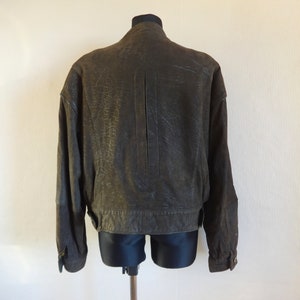 Puede incluir: Una chaqueta de cuero marr&oacute;n con cierre de cremallera y cuello alto. La chaqueta tiene una superficie texturizada y una longitud ligeramente recortada.