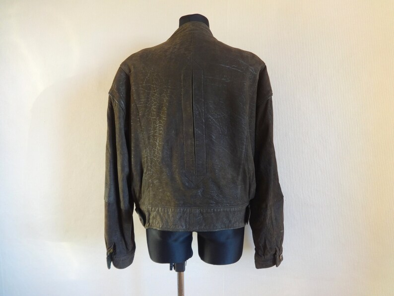 Puede incluir: Una chaqueta de cuero marr&oacute;n con cierre de cremallera y cuello alto. La chaqueta tiene una superficie texturizada y una longitud ligeramente recortada.