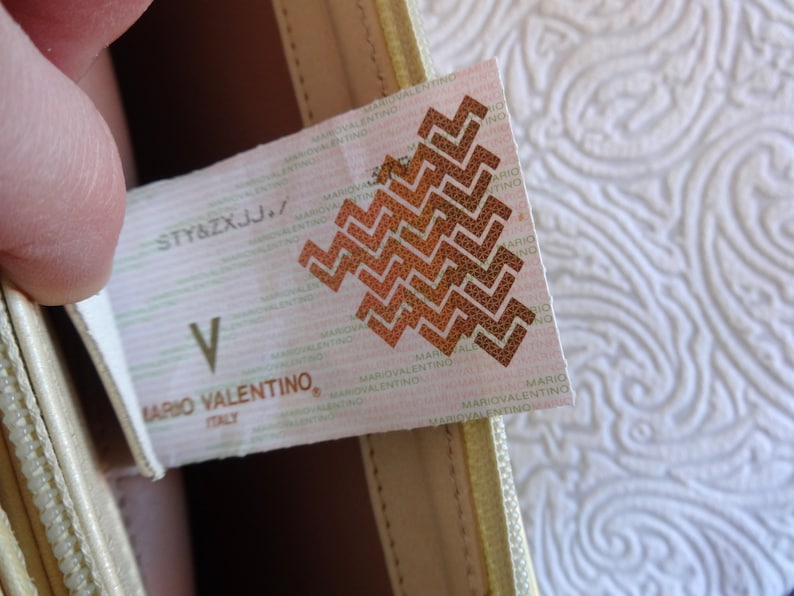 May include: A white tag with the text "STY&ZXJJ." and "MARIO VALENTINO, ITALY" printed on it. The tag also features a brown geometric pattern.
