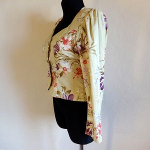 Puede incluir: Chaqueta verde claro con estampado floral y mangas largas. La chaqueta presenta un escote en V y est&aacute; adornada con un patr&oacute;n de flores rojas, moradas y blancas. La prenda se exhibe en un maniqu&iacute; negro.