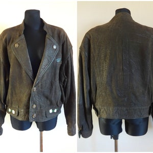 Puede incluir: Una chaqueta de cuero marr&oacute;n con cierre de cremallera y detalles de botones. La chaqueta tiene un aspecto desgastado y presenta flores blancas bordadas en el dobladillo inferior.