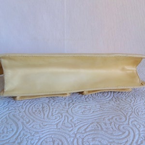 May include: A pale yellow leather handbag with a single strap. The bag has a flap closure and multiple compartments.