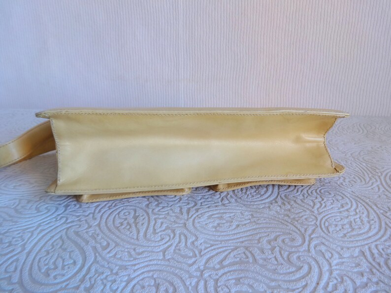 May include: A pale yellow leather handbag with a single strap. The bag has a flap closure and multiple compartments.