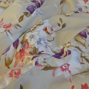 Puede incluir: Tela beige con un estampado floral con flores rosas, moradas y blancas y hojas marrones. La tela est&aacute; drapeada, mostrando la textura y el dise&ntilde;o. La prenda tiene botones blancos.