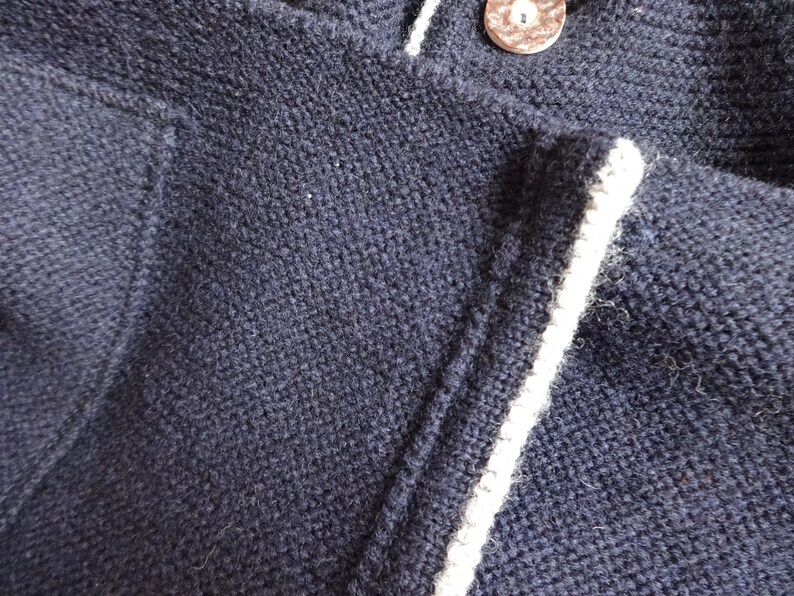 Puede incluir: Primer plano de un su&eacute;ter de punto azul marino con ribetes blancos. El su&eacute;ter tiene un cierre de bot&oacute;n y una textura acanalada.