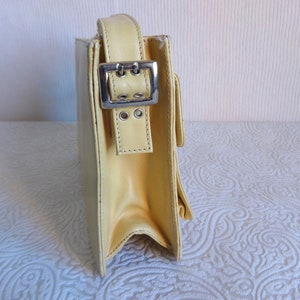 May include: A pale yellow leather shoulder bag with a silver buckle and strap. The bag has a flap closure and a structured shape.