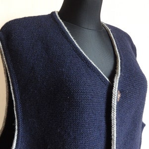 Puede incluir: Un chaleco de punto azul marino con ribete gris alrededor del cuello y la abertura de botones. El chaleco tiene cuello en V y un solo cierre de bot&oacute;n.