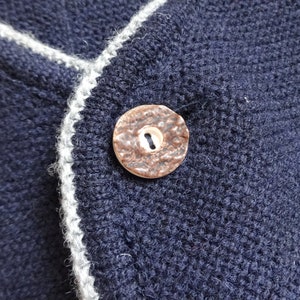Puede incluir: Primer plano de una tela de punto azul oscuro con ribete blanco. Un bot&oacute;n marr&oacute;n con un solo agujero est&aacute; cosido en la tela.