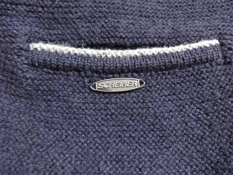 Puede incluir: Un su&eacute;ter azul marino con ribete blanco y una etiqueta de metal plateado que dice "SCHEIBER".