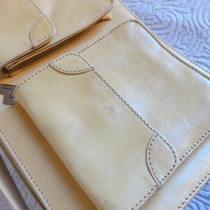 May include: A light beige leather bag with multiple pockets and a zipper closure. The bag has a flap with a metal clasp.