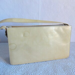 May include: A pale yellow leather shoulder bag with a zipper closure. The bag has a strap and is made of a smooth, soft leather.