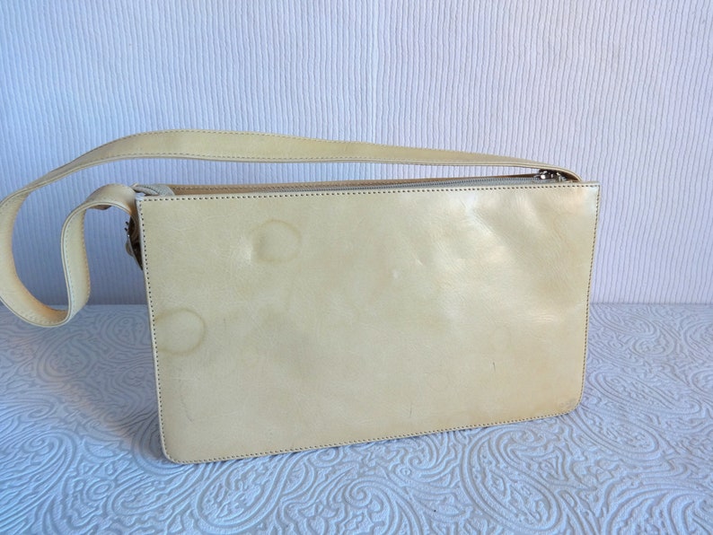 May include: A pale yellow leather shoulder bag with a zipper closure. The bag has a strap and is made of a smooth, soft leather.