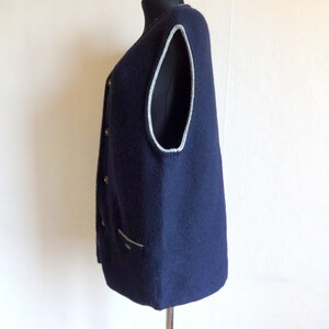 Puede incluir: Un chaleco de punto azul marino con ribete gris claro alrededor de las sisas y el escote. El chaleco tiene cierre de botones y un bolsillo en la parte delantera.