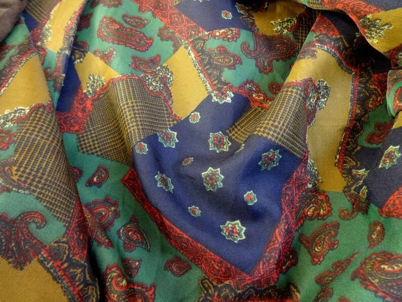 Puede incluir: Una tela colorida con un patr&oacute;n de paisley en tonos de verde, azul, rojo y dorado. La tela est&aacute; doblada y drapeada, mostrando los diferentes patrones y colores.