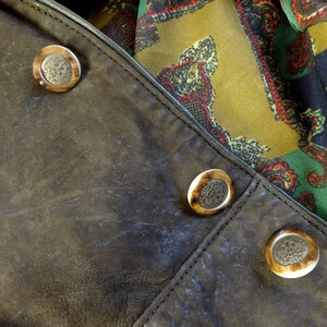 Puede incluir: Primer plano de una chaqueta de cuero marr&oacute;n con tres botones decorativos. Los botones son redondos y tienen un color marr&oacute;n claro con un centro marr&oacute;n oscuro.