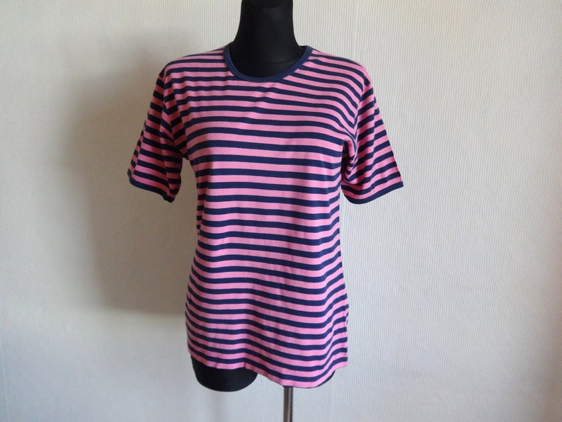 K&ouml;nnte beinhalten: Ein pinkfarbenes und marineblaues gestreiftes T-Shirt mit kurzen &Auml;rmeln und einem Rundhalsausschnitt.