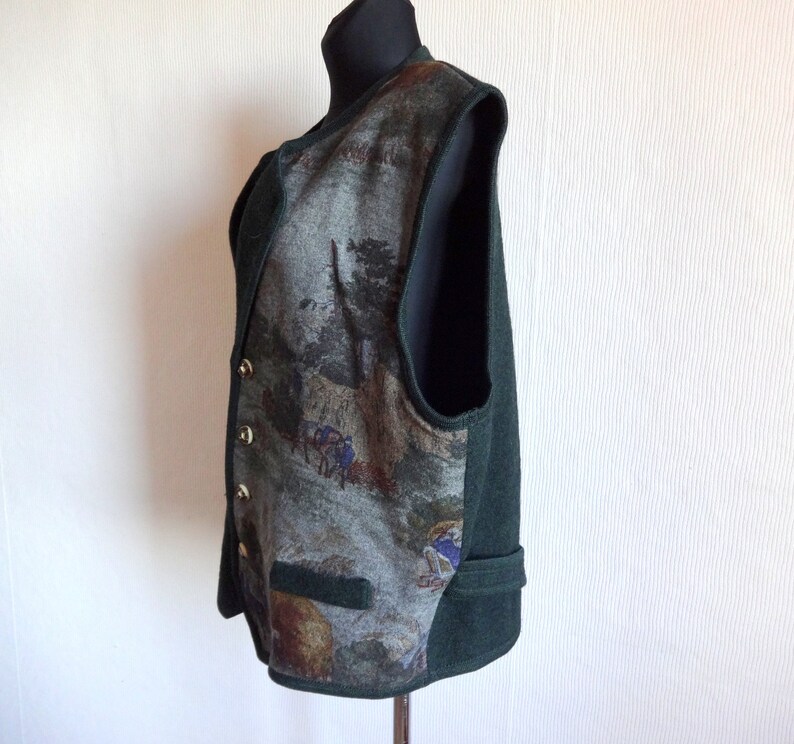 Puede incluir: Un chaleco verde sin mangas con un frente estampado que representa una escena de bosque. El chaleco tiene cierre de botones y un bolsillo en la parte delantera.