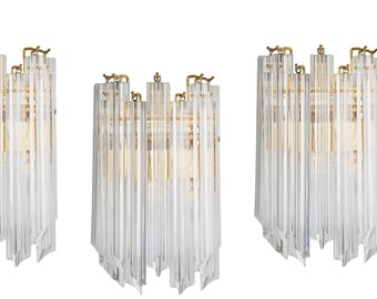 Peut inclure: Trois appliques murales dorées avec des tiges en cristal de verre clair. Les appliques sont disposées en rangée et sont éclairées par une lumière blanche chaude.