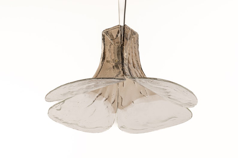 May include: A clear glass pendant light fixture with a flower-shaped design. The fixture has a brown, textured glass shade and four clear glass petals.
