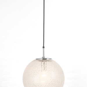 Peut inclure: Un luminaire suspendu en forme de globe blanc avec un cordon noir et une fixation au plafond chrom&eacute;e. Le globe pr&eacute;sente un motif d&eacute;licat et textur&eacute;.