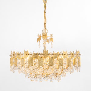 Peut inclure: Un lustre dor&eacute; avec des gouttes de cristal claires et un design circulaire. Le lustre est dot&eacute; d'une cha&icirc;ne dor&eacute;e et d'une fixation au plafond dor&eacute;e.