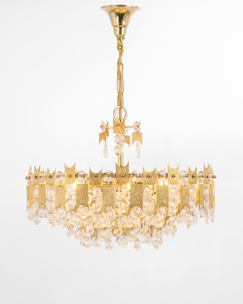 Peut inclure: Un lustre dor&eacute; avec des gouttes de cristal claires et un design circulaire. Le lustre est dot&eacute; d'une cha&icirc;ne dor&eacute;e et d'une fixation au plafond dor&eacute;e.