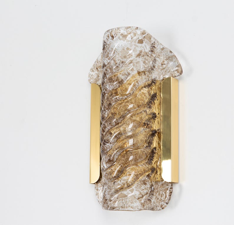 May include: A brass wall sconce with a textured glass shade. The glass is clear with a brown tint and has a swirling pattern.