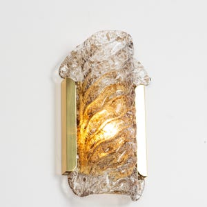 May include: A brass wall sconce with a clear and brown glass shade. The glass shade has a textured, swirling design.
