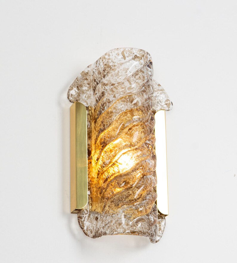 May include: A brass wall sconce with a clear and brown glass shade. The glass shade has a textured, swirling design.