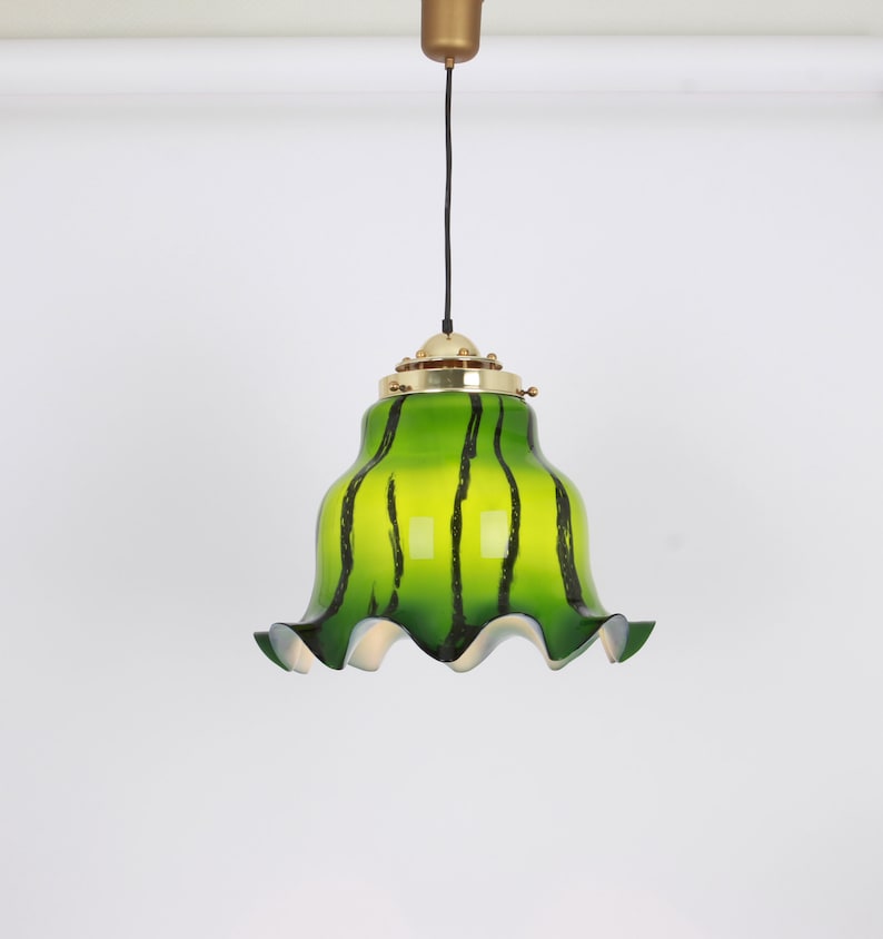 May include: A green glass pendant light with black stripes and a ruffled edge. The light is hanging from a black cord and a gold metal ceiling fixture.