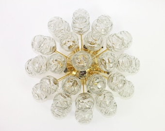 May include: A brass and glass chandelier with multiple clear glass bulbs. The bulbs have a textured, rippled surface. The chandelier has a circular shape and is designed to be mounted on a wall.