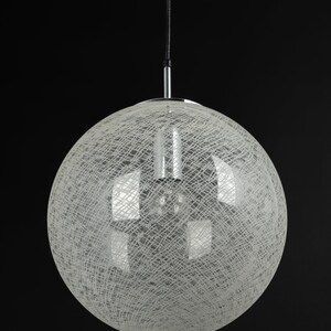 Peut inclure: Un luminaire rond blanc suspendu avec un motif d&eacute;licat tiss&eacute;. Le luminaire est suspendu &agrave; un cordon noir et a une finition chrom&eacute;e.