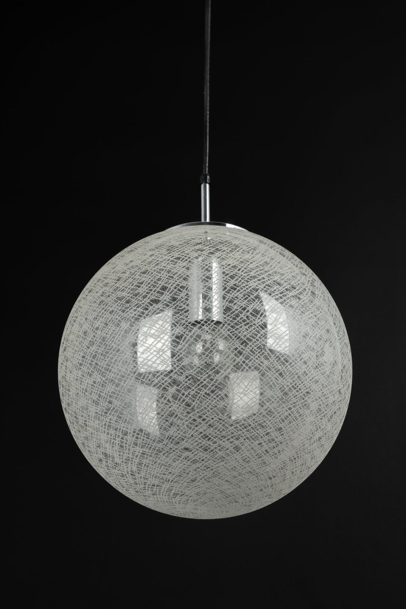 Peut inclure: Un luminaire rond blanc suspendu avec un motif d&eacute;licat tiss&eacute;. Le luminaire est suspendu &agrave; un cordon noir et a une finition chrom&eacute;e.