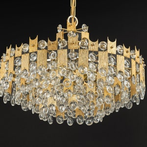 Peut inclure: Un lustre de couleur or avec un design g&eacute;om&eacute;trique et des gouttes de cristal claires. Le lustre a une forme circulaire et est fait de m&eacute;tal.