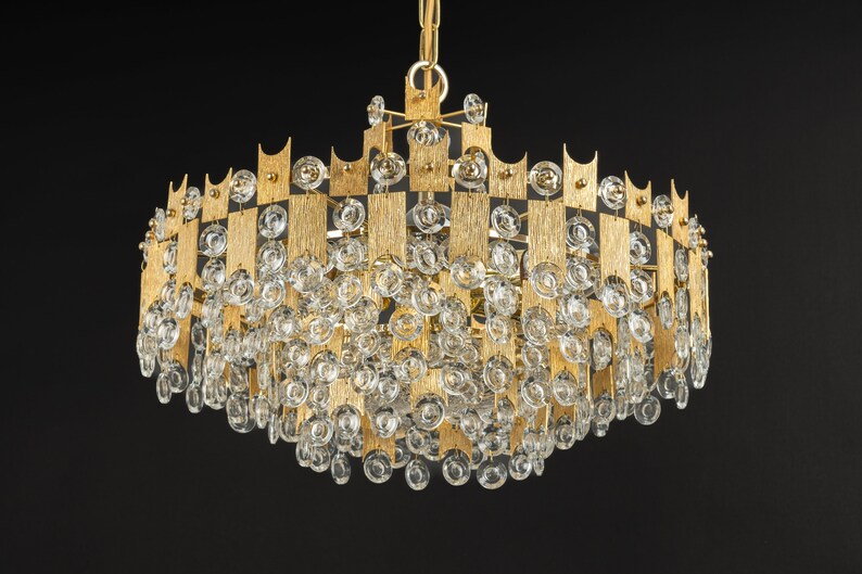 Peut inclure: Un lustre de couleur or avec un design g&eacute;om&eacute;trique et des gouttes de cristal claires. Le lustre a une forme circulaire et est fait de m&eacute;tal.