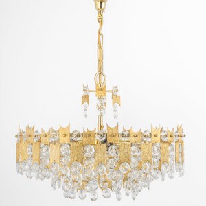 Peut inclure: Un lustre de couleur or avec un design circulaire et des gouttes de cristal claires. Le lustre a une finition en m&eacute;tal martel&eacute; textur&eacute;.