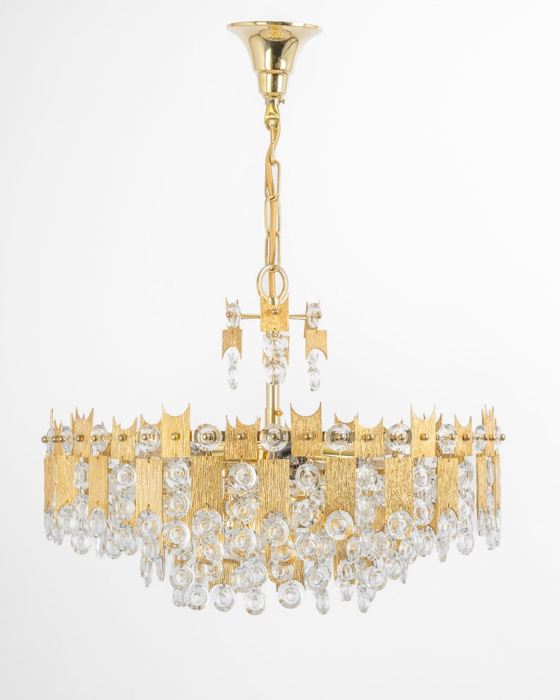 Peut inclure: Un lustre de couleur or avec un design circulaire et des gouttes de cristal claires. Le lustre a une finition en m&eacute;tal martel&eacute; textur&eacute;.
