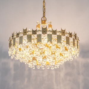 Peut inclure: Un lustre dor&eacute; avec un cadre circulaire et des gouttes de cristal en cascade. Le lustre a un design g&eacute;om&eacute;trique avec une s&eacute;rie de barres verticales.