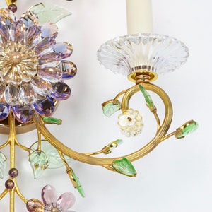 Puede incluir: Una l&aacute;mpara de pared dorada con un dise&ntilde;o de flor de cristal. La l&aacute;mpara tiene una sola bombilla y est&aacute; decorada con cristales verdes y morados.
