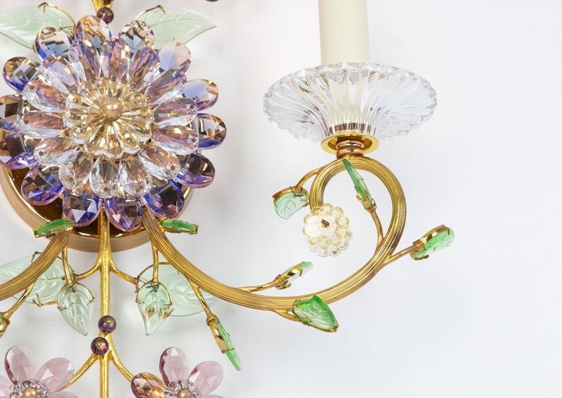 Puede incluir: Una l&aacute;mpara de pared dorada con un dise&ntilde;o de flor de cristal. La l&aacute;mpara tiene una sola bombilla y est&aacute; decorada con cristales verdes y morados.
