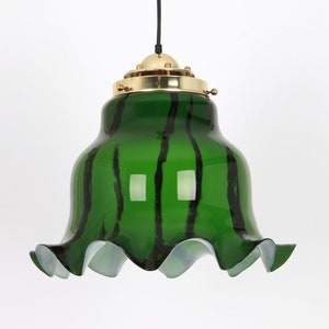 May include: A green glass pendant light with black stripes and a ruffled edge. The light fixture has a brass top with a decorative design.