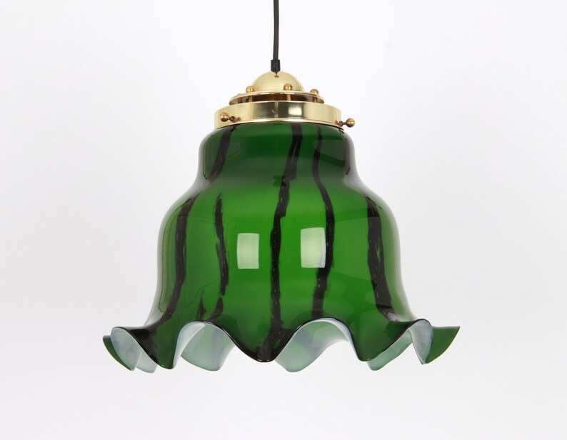 May include: A green glass pendant light with black stripes and a ruffled edge. The light fixture has a brass top with a decorative design.