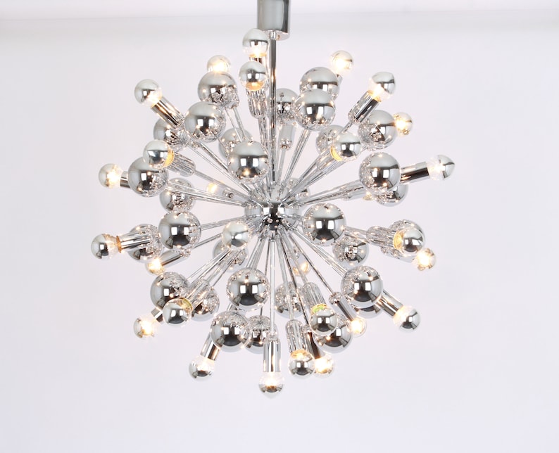 Op de afbeelding: Een chromen Sputnik-kroonluchter met meerdere lampen. De kroonluchter heeft een stervormig ontwerp met veel armen die naar buiten uitstrekken.