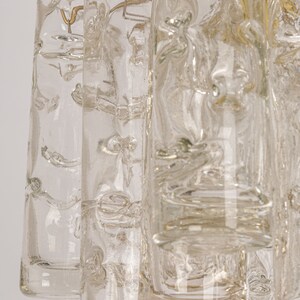 May include: A close-up of a clear glass chandelier with a textured surface. The chandelier has multiple tiers of glass cylinders.